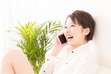 Oturma odasında cep telefonuyla konuşan güzel genç bir Japon kadın.