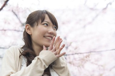 Parkta çiçek açan sakura ağaçlarıyla poz veren genç Asyalı kadın.