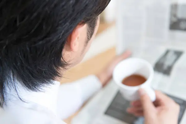 asian young man reading a newspaper with cup of coffee