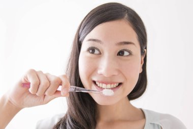 Diş fırçasıyla diş temizleyen genç Asyalı kadın.