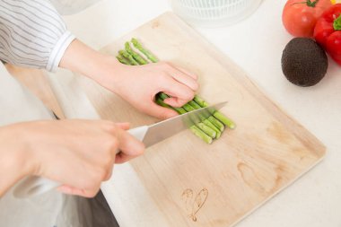 Mutfak tahtasında kuşkonmaz doğrayan kadın.