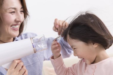 Saç kurutma makinesiyle Asyalı anne ve kızı. 