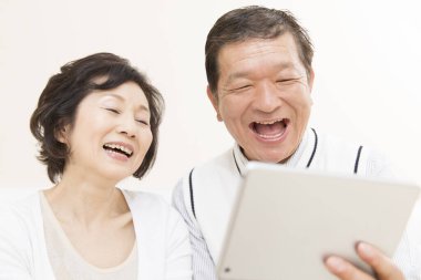 Evde tabletleri olan yaşlı Japon bir çiftin portresi.