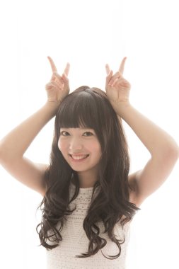 Genç Asyalı kadın gülümseyerek boynuzlarını parmaklarıyla gösteriyor.