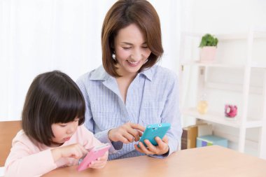 gülümseyen Asyalı anne-kız telefonları kullanıyor.