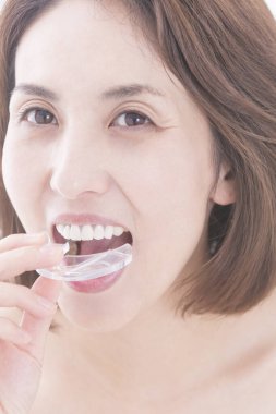 Güzel, olgun Japon bir kadının beyaz arka planda dişlerini beyazlatırken yakın plan fotoğrafı.