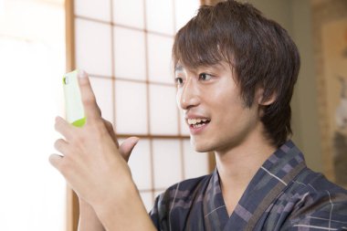 Geleneksel Yukata 'daki yakışıklı Japon genç adamın portresi. Etnik kaplıca otelinde akıllı telefon kullanıyor.