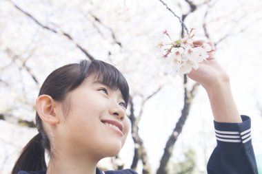 Sokakta çiçek açan kiraz ağaçlarıyla güzel Japon öğrencinin portresi.