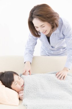 Asyalı kız uyuyor, annesi yanında duruyor.