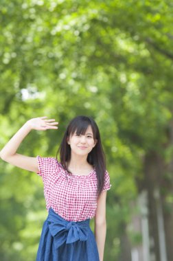 Genç bir kadın yaz parkında el sallıyor.