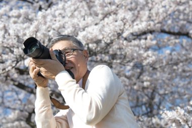 Olgun Asyalı fotoğrafçı parkta fotoğraf çekiyor.