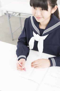 Okul üniformalı gülümseyen Japon öğrenci okulda ders çalışıyor.