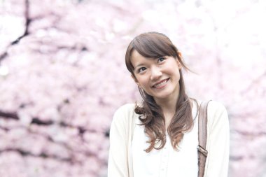 Parkta çiçek açan sakura ağaçlarıyla poz veren genç Asyalı kadın.