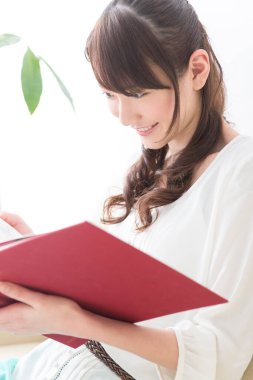 Asyalı kadın evde kitap okuyor.