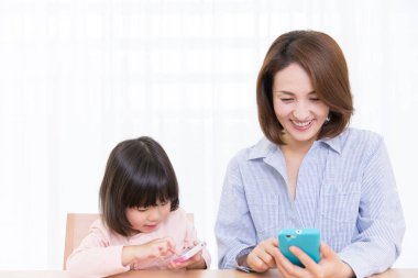 gülümseyen Asyalı anne-kız telefonları kullanıyor.