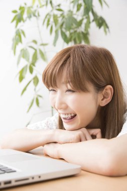 Evde gülümseyen ve laptop kullanan bir kadın.