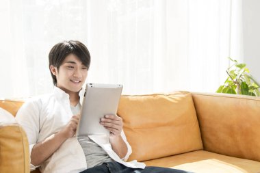 Genç Asyalı iş adamı oturma odasında tablet bilgisayar kullanıyor.