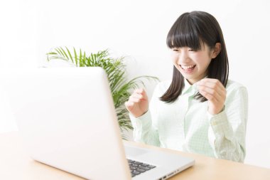 Gülümseyen Japon kız dizüstü bilgisayarla masada oturuyor.