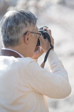 Olgun Asyalı fotoğrafçı parkta fotoğraf çekiyor.