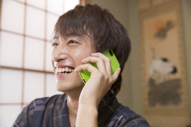 Geleneksel Yukata 'daki yakışıklı Japon genç adamın portresi. Etnik kaplıca otelinde akıllı telefon kullanıyor.