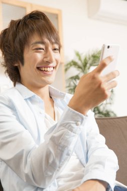 Genç Asyalı adam evde akıllı telefon kullanıyor.. 