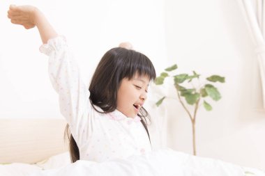 Asyalı küçük kız yatakta kolalanıyor.