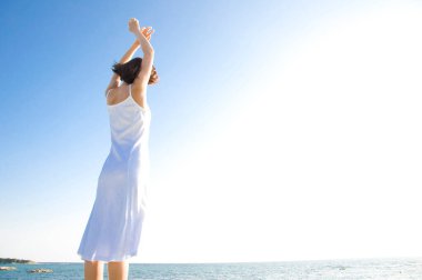 Kolları havada, kumsalda eğlenen mutlu kadın.