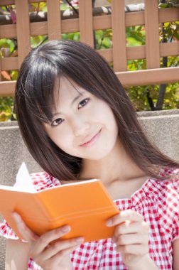 Açık havada kitap okuyan Asyalı genç kızın portresi.