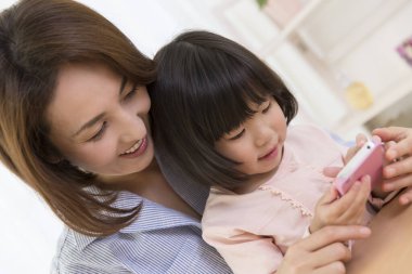 Asyalı anne ve kızı telefon kullanıyor.