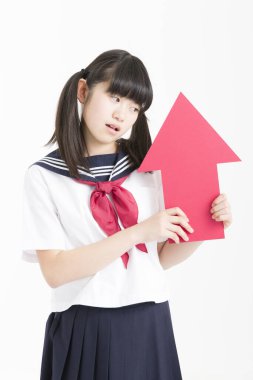 Okul üniformalı küçük Asyalı kız elinde kırmızı ok işareti var, beyaz arka planda izole edilmiş.