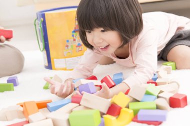 Küçük sevimli Asyalı kız tahta oyuncak bloklarıyla oynuyor.