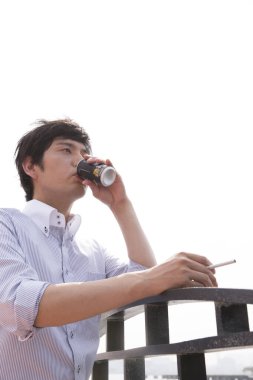 Genç Asyalı adam açık havada içiyor. 