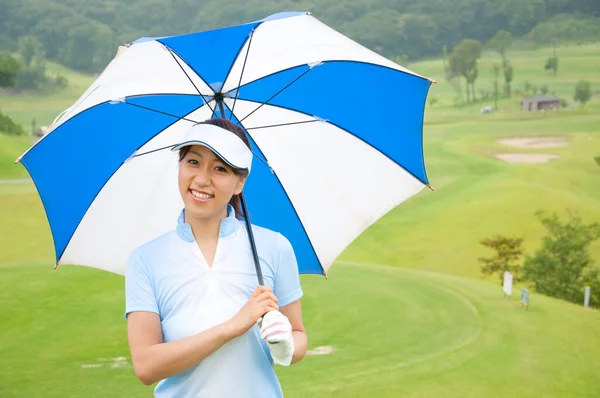 アジアの女性ゴルフプレーヤーが青と白の傘でポーズ — ストック写真