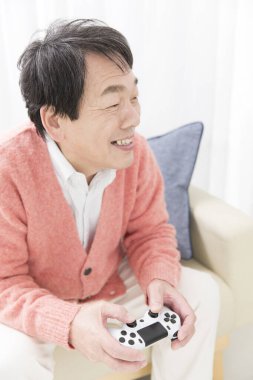 Asyalı son sınıf öğrencisi kanepede video oyunu oynuyor.