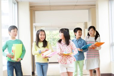 Okul koridorunda yürüyen kitaplarla bir grup Japon çocuk. 