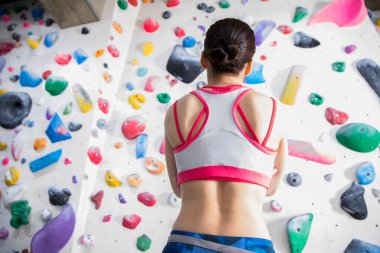 Genç kadın tırmanma duvarının yanında duruyor.
