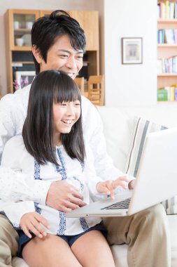 Evde dizüstü bilgisayar kullanan mutlu bir Asyalı aile.