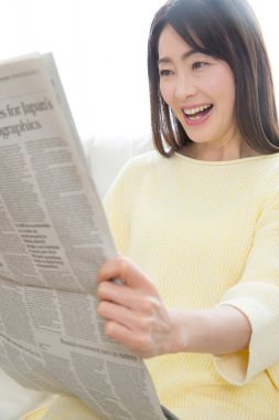 Evde gazete okuyan güzel Asyalı kadının portresi.