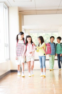 Okul koridorunda sırt çantalı bir grup Japon çocuk yürüyor. 
