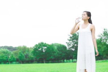 Yeşil yaz parkında gündüz vakti su içen güzel Japon kadın. 
