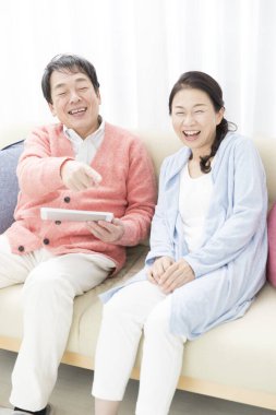 Mutlu yaşlı çift evde tabletleriyle kanepede oturuyor.