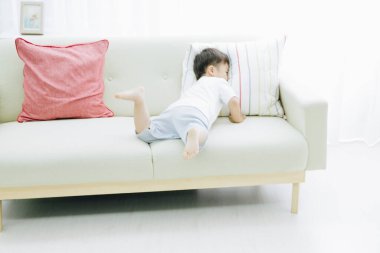 Evdeki kanepede oturan Asyalı küçük çocuğun portresi.