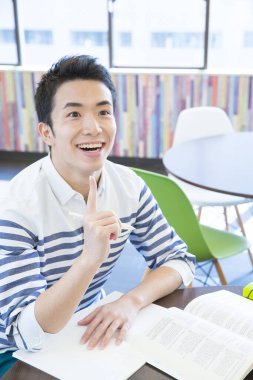 Asyalı öğrenci üniversitede masa başında okuyor. 