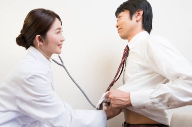 Asyalı doktor steteskopla bir hastayı muayene ediyor.