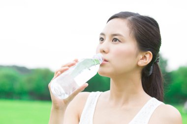 Yeşil yaz parkında gündüz vakti su içen güzel Japon kadın. 