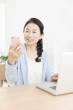 Asyalı son sınıf öğrencisi evde akıllı telefon ve laptop kullanıyor. 