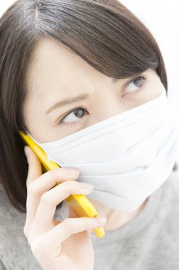 Asyalı kadın akıllı telefon kullanarak yüz maskesi takıyor. 