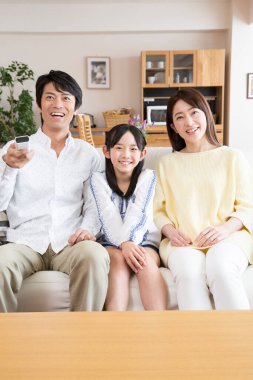 Genç bir aile kanepede oturup televizyon seyrediyor.