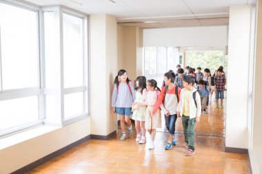 Okul koridorunda sırt çantalı bir grup Japon çocuk yürüyor. 