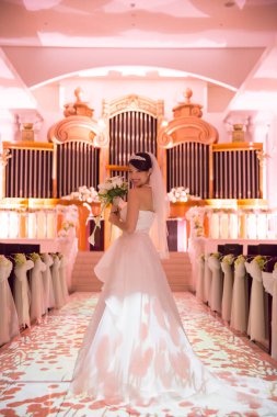 Kilisede duran beyaz elbiseli gelinin portresi.